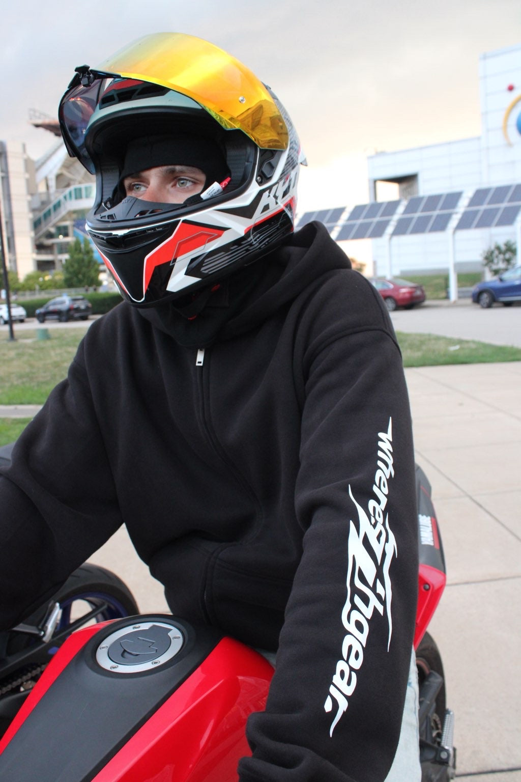 Close-up of a rider in a black WHERES7THGEAR hoodie and helmet with orange visor