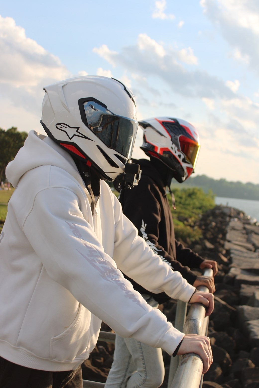 Two riders leaning against a railing by water at sunset